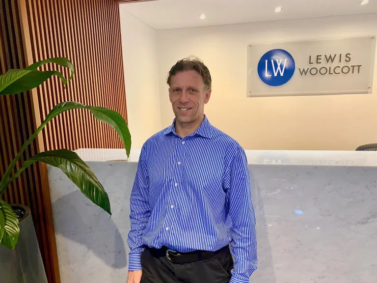 Business man standing in the reception area of the new Lewis Woolcott Perth office with the business logo on the wall behind.